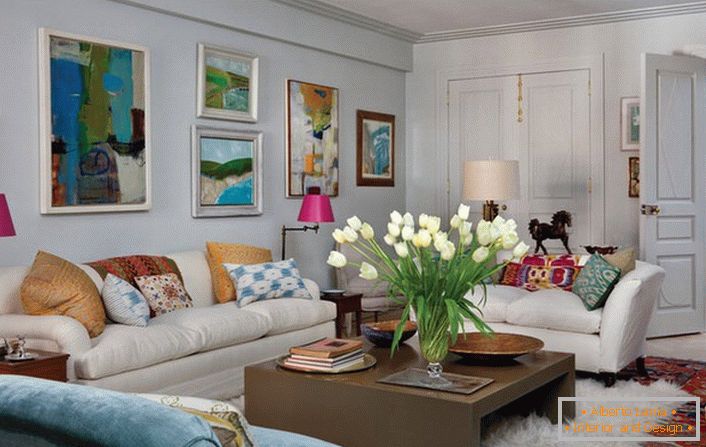 Sala de estar universal em estilo eclético. Uma sala aconchegante faz muitos travesseiros e pinturas abstratas e brilhantes que adornam a parede acima do sofá.