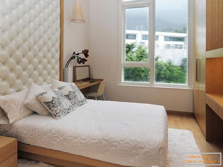 Uma pequena cama com cabeceira de couro e no quarto com uma grande janela