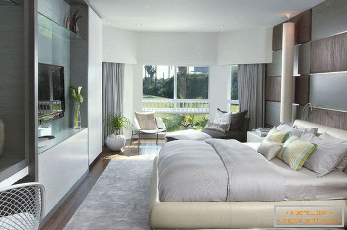 Cama macia e volumosa no quarto em estilo moderno. Mobiliário com uma superfície brilhante se encaixa bem com a composição geral do interior.