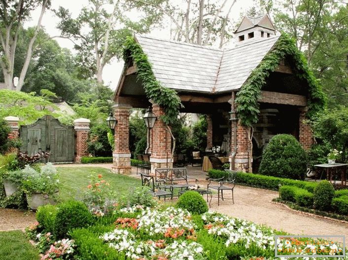 A simplicidade elegante de um gazebo aberto no estilo de um chalé parece organicamente em um jardim luxuoso e aconchegante. 