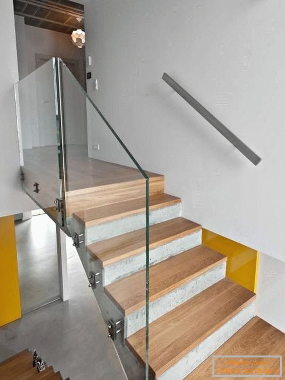 Escada de concreto com degraus de madeira e trilhos de vidro em uma casa particular