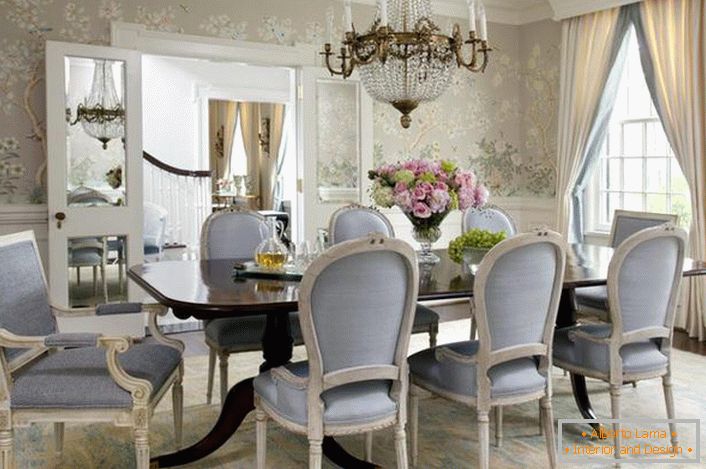 A sala de jantar no estilo neoclássico é decorada em tons de azul claro e cinza claro. Papel de parede de flores olhar suavemente em combinação com plintos altos brancos.