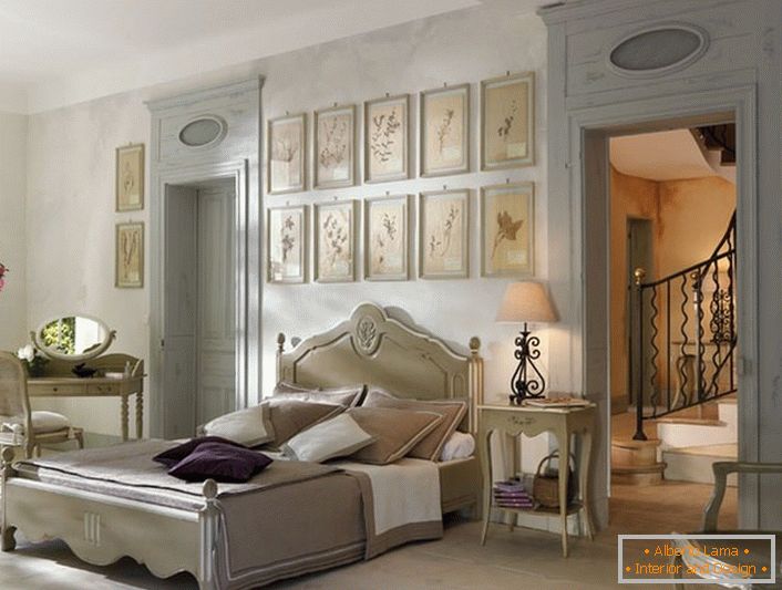 De acordo com as tradições do estilo francês para o quarto foi selecionado móveis de luz lacônica de madeira. Um detalhe interessante é uma colagem de fotos acima da cabeceira da cama.