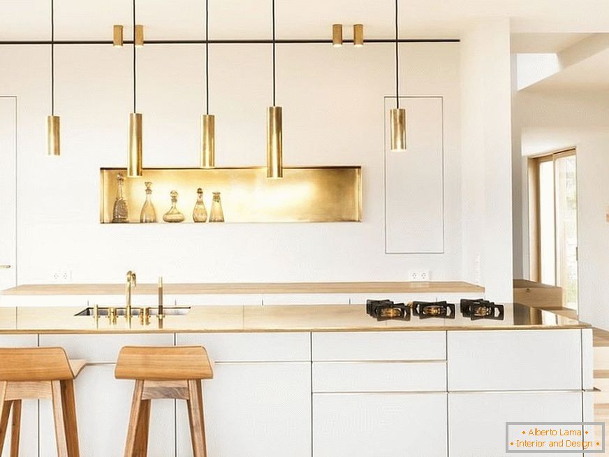 Elementos de decoração dourada em uma cozinha branca com bancos de bar de madeira