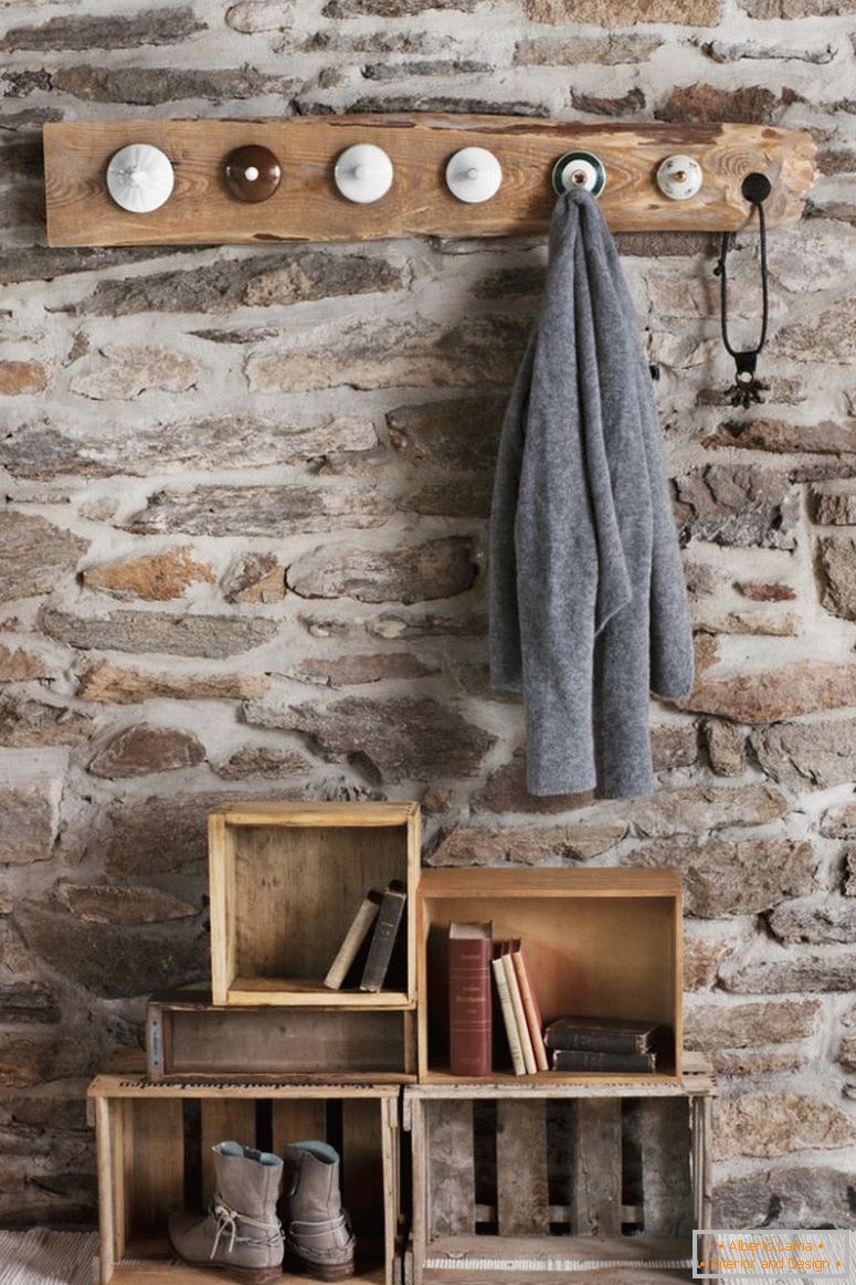 Bengaleiro rústico de bricolage no quarto com muro de pedra; cabides de casaco feitos de tampas de porcelana velha e caixas de madeira velhas no chão como armazenamento