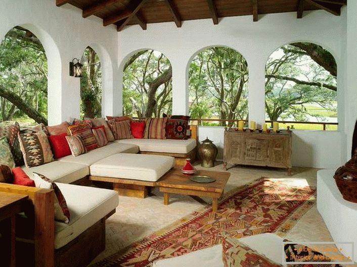 A varanda da casa de campo é decorada de acordo com o estilo mediterrâneo. Uma característica interessante é a decoração com muitas almofadas coloridas.