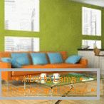 Sofá laranja com almofadas azuis contra o fundo da parede de pistache