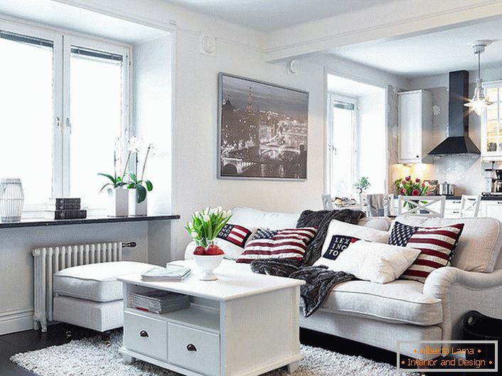 Um acolhedor apartamento em estilo escandinavo é decorado principalmente em branco. Janelas sem cortinas permitem que a luz do dia seja suficiente para entrar na sala.