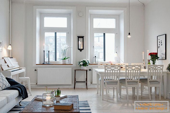 A elegante sala de estar está dividida em uma área de estar e área para refeições. De acordo com o estilo escandinavo, as paredes da sala são decoradas em branco.