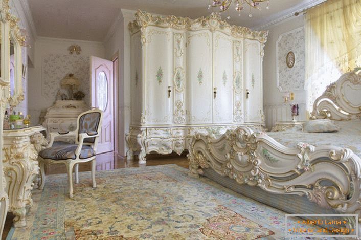 Quarto branco como a neve, com móveis maciços esculpidos em madeira. A cama com uma cabeceira alta na cabeceira da cama, elegantemente se encaixa no interior em estilo barroco.