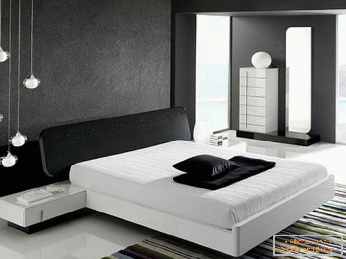 A parede na cabeceira da cama, decorada com uma inserção mate cinza, de acordo com o estilo da alta tecnologia, está em harmonia com o piso branco brilhante.