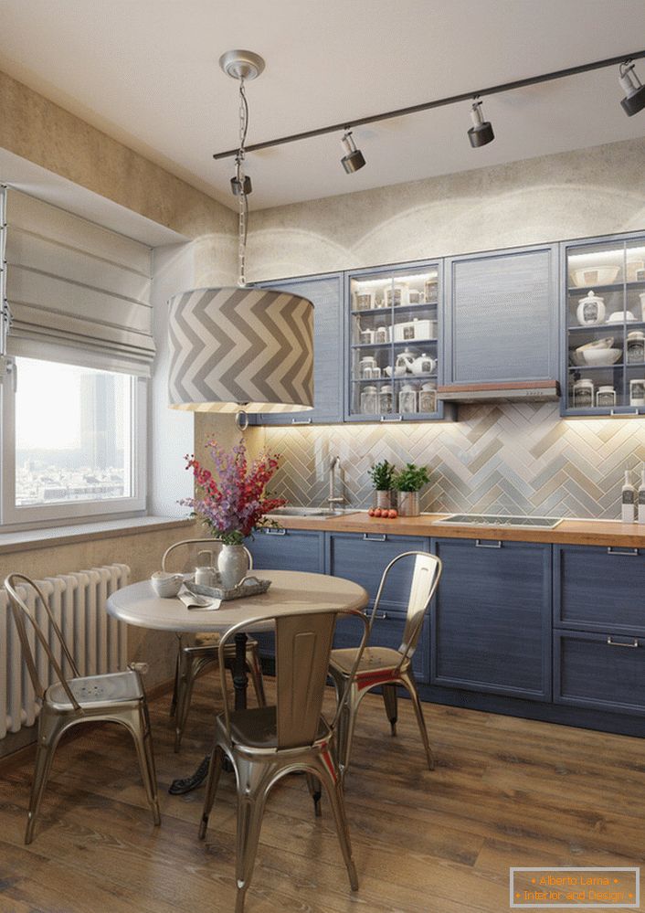A cor azul pálida do conjunto de cozinha é uma excelente solução para a culinária eclética. Um exemplo de iluminação perfeitamente selecionada, que ilumina separadamente a área de trabalho e a mesa de jantar.