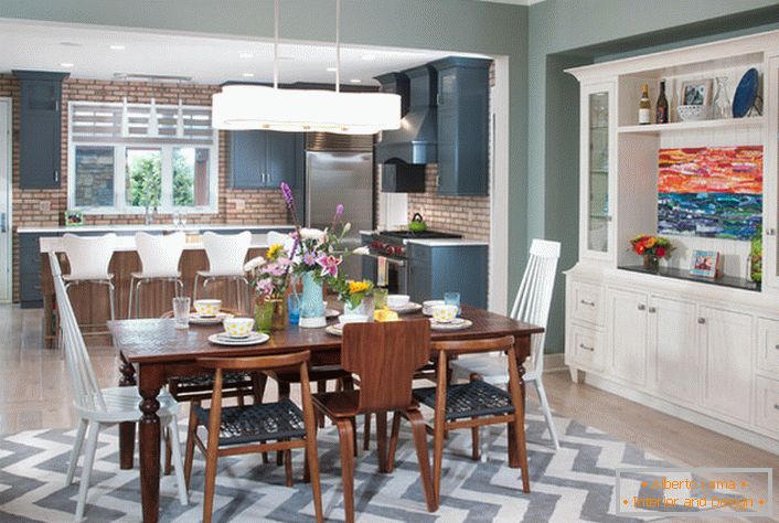Uma grande cozinha de estilo eclético é dividida em uma área de trabalho e de jantar. A mobília da cor branca combina-se com elementos de um interior da cor marrom-escura.